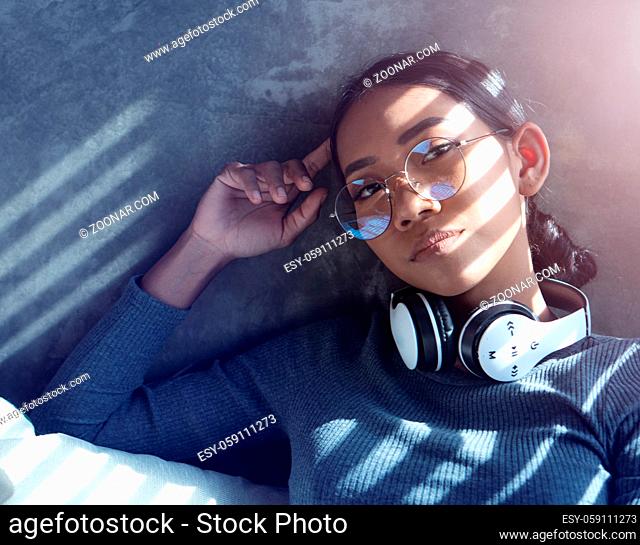 Portrait of attractive girl with headphones sitting on the sofa by the window at home. People, comfortable lifestyle and leisure concept