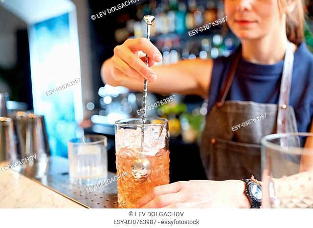 alcohol drinks, people and luxury concept - woman bartender with stirrer and glass preparing cocktail at bar counter
