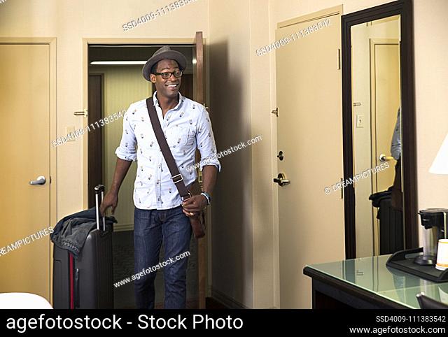 Black man with rolling suitcase entering hotel room
