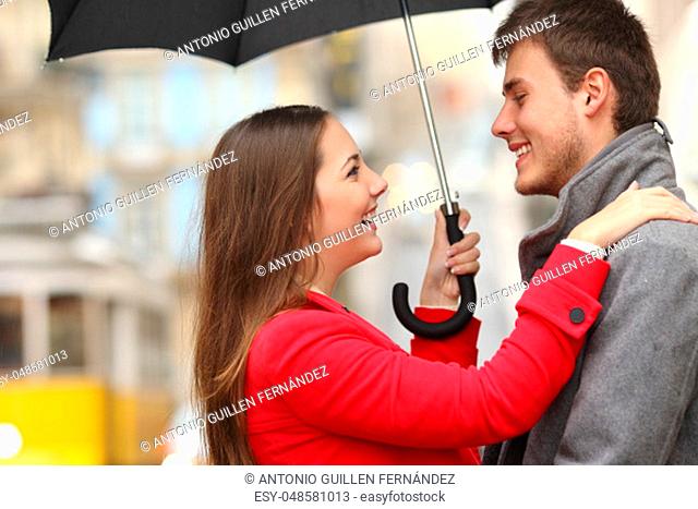 Side view of a couple encounter in the street under an umbrella in a rainy day