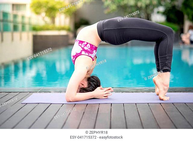 Beautiful young Asian woman doing yoga exercise near swimming pool. Healthy lifestyle and good wellness concepts