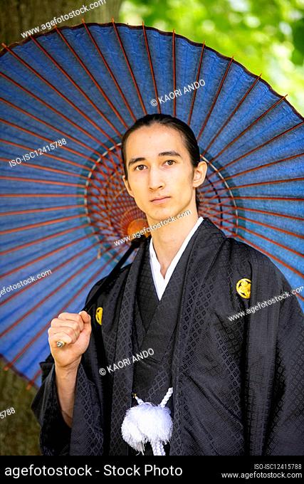 UK, Portrait of young man wearing kimono holding parasol in park