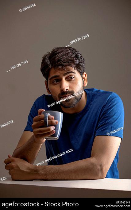 A YOUNG MAN SITTING AND THINKING WHILE HOLDING COFFEE MUG