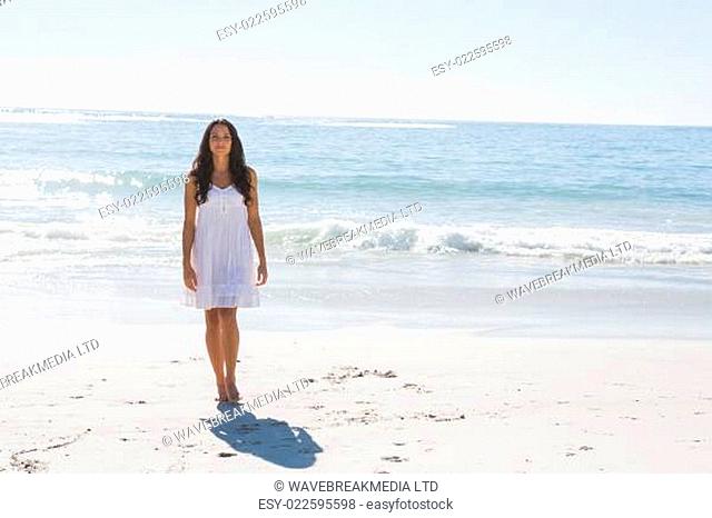 Beautiful brunette in white sun dress walking from the ocean