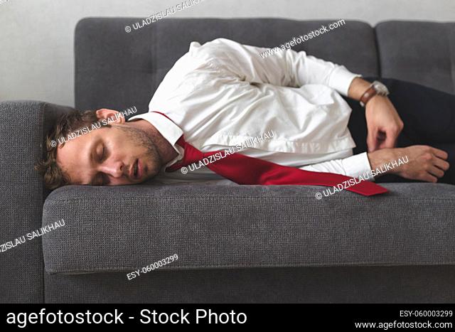Tired overworked businessman deeply sleep on sofa. He slept all night on the couch in office clothes