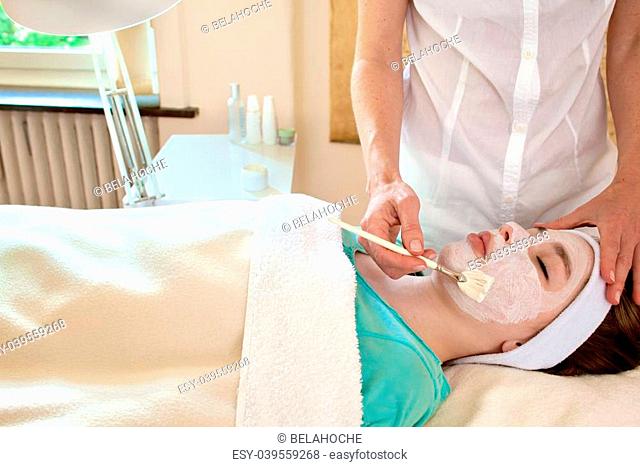 Alternative practitioner applying a chemical peel to a female patient's face in a beauty clinic
