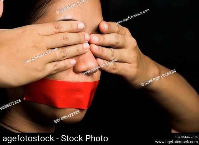 Asian woman blindfold wrapping mouth with red adhesive tape on black background. Freedom speech censorship and stop talk, International Human Right day