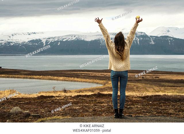 Iceland, woman standing at lakeside with raised arms