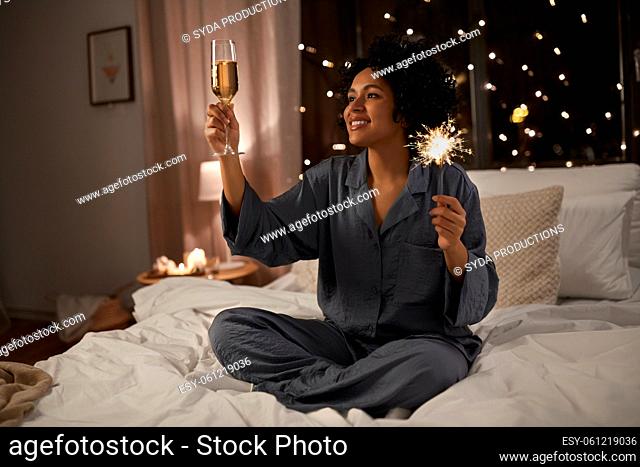 happy woman drinking champagne in bed at night