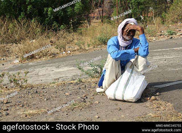 An old man tired of walking is seated on a road side. India
