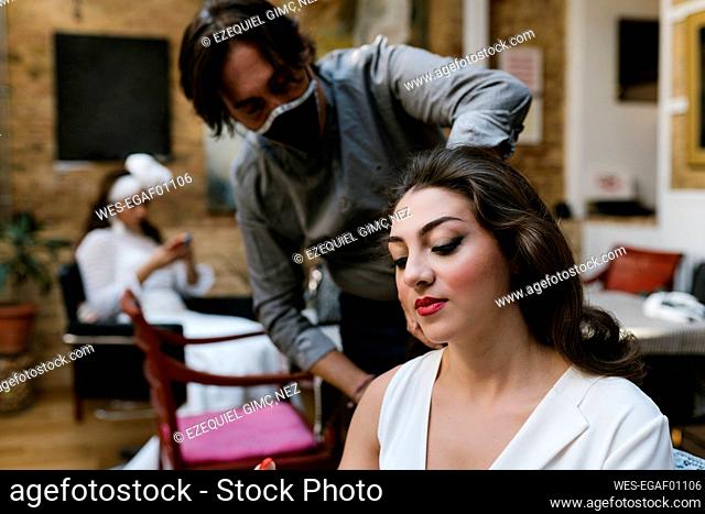 Mature male hairdresser preparing bride for wedding during COVID-19