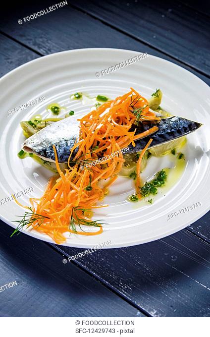 Blue mackerel fish fillet with aubergines and carrots drizzled with olive oil and garnished with dill and herbs on a white plate