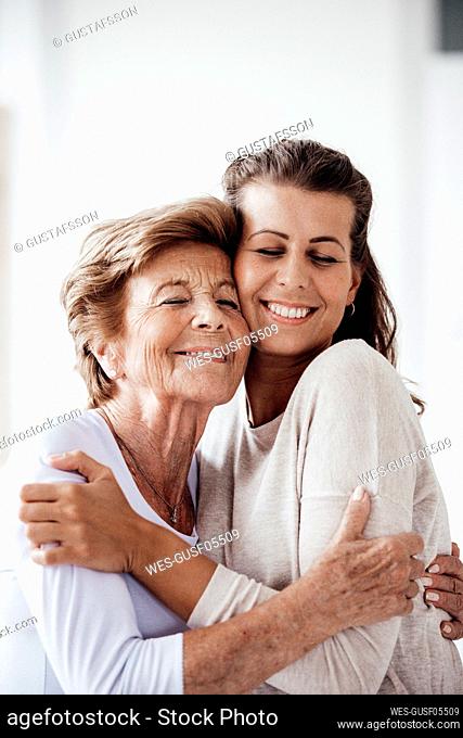 Smiling woman and granddaughter embracing each other at home