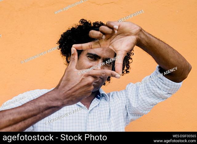 Man making finger frame in front of beige wall