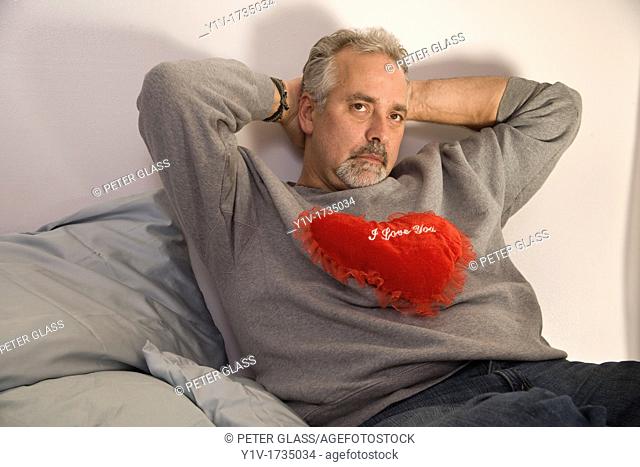 Middle-age man holding a heart-shaped pillow with 'I Love You' written on it