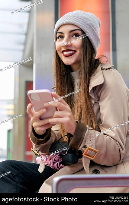 Contemplating woman in warm clothing holding smart phone