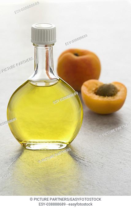 Glass bottle with cosmetic apricot kernel oil and fresh apricots on the background