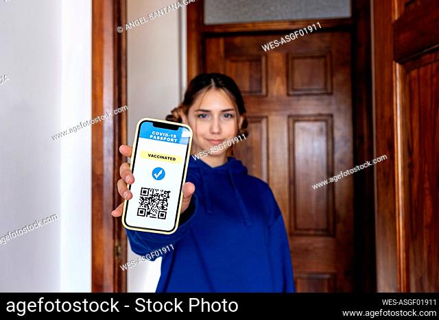 Mujer joven que muestra un certificado de vacuna digital en un teléfono inteligente en casa