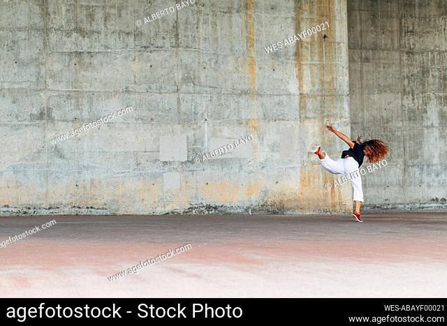 Young woman doing acrobatic jump while exercising against wall