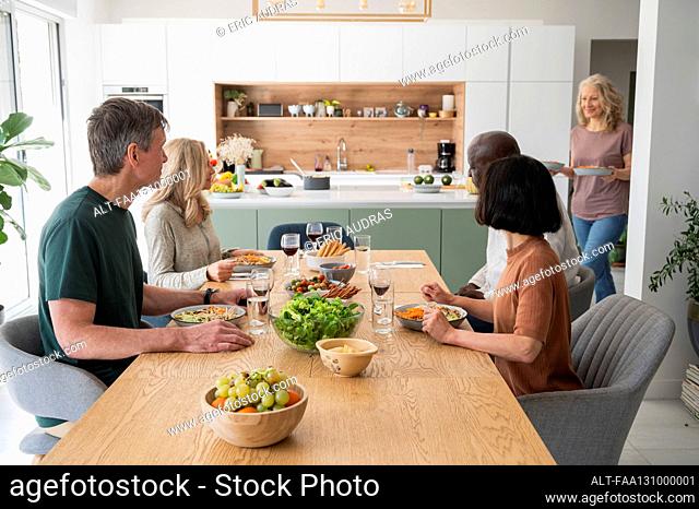 Group of diverse middle age friends gathered for dinner in kitchen