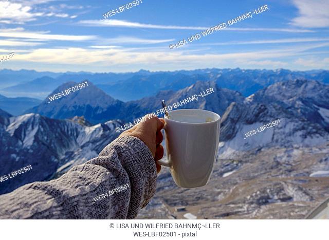 Germany, Bavaria, Zugspitze, hand holding coffee mug in mountain panorama