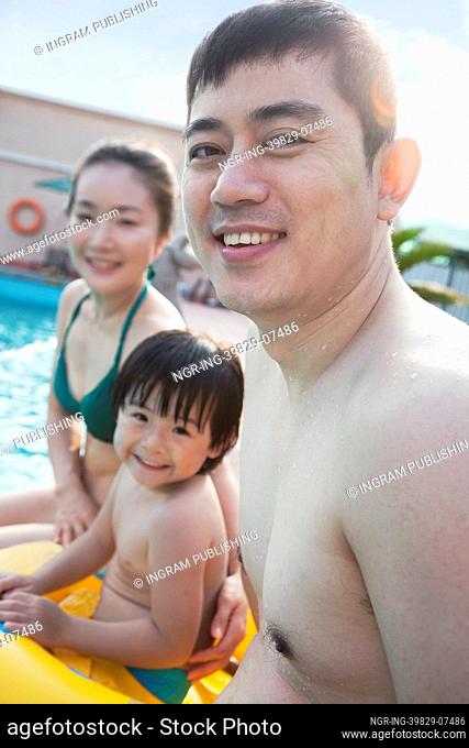 Portrait of smiling happy family sitting by the pool