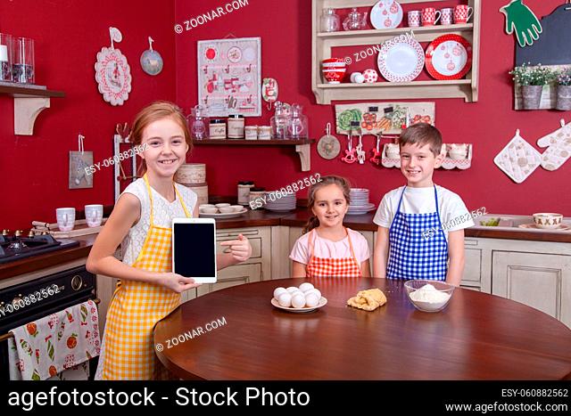 Children in the kitchen trying to learn cooking. Best friends in aprons holding pastry in their hands and making cake in kitchen and looking at each other
