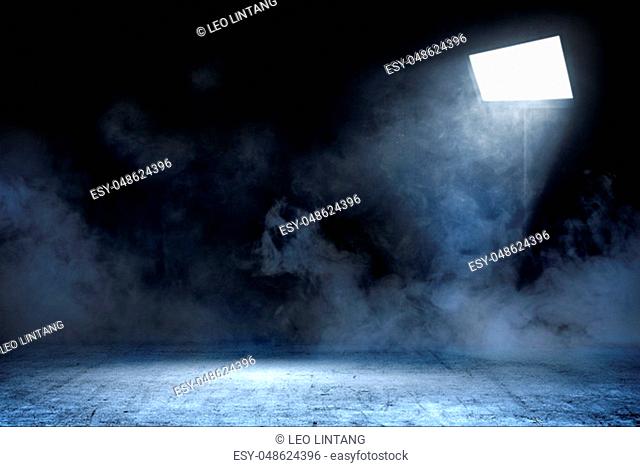 Room with concrete floor and smoke with light from spotlights against dark wall background