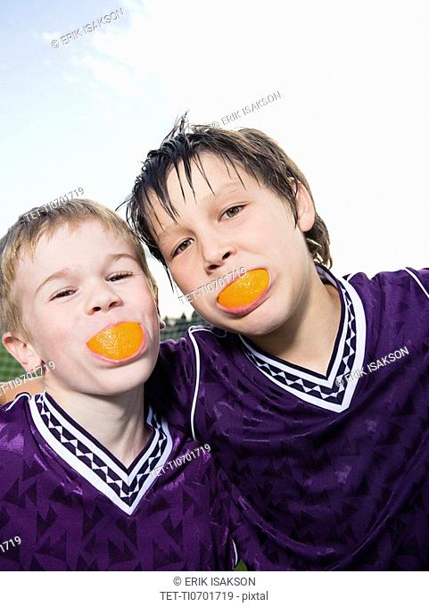 Portrait of boys in soccer uniforms with orange wedges in mouth
