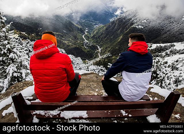 Friends spending leisure time sitting on bench during winter
