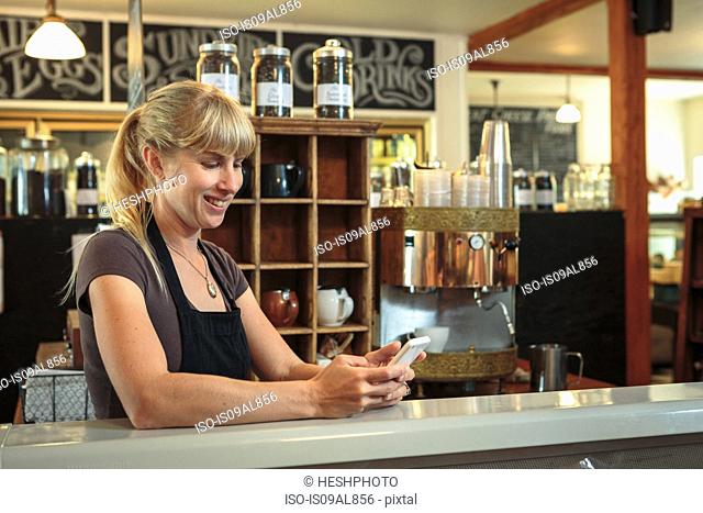 Female shop assistant texting on smartphone in country store cafe