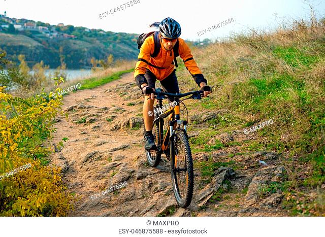 Cyclist in Orange Riding the Mountain Bike on the Autumn Rocky Trail. Extreme Sport and Enduro Biking Concept