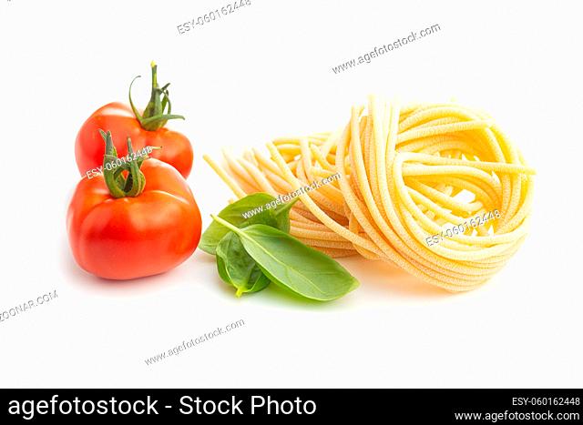 Italian pasta nest, tomato and basil leaves. Uncooked spaghetti nest isolated on white background