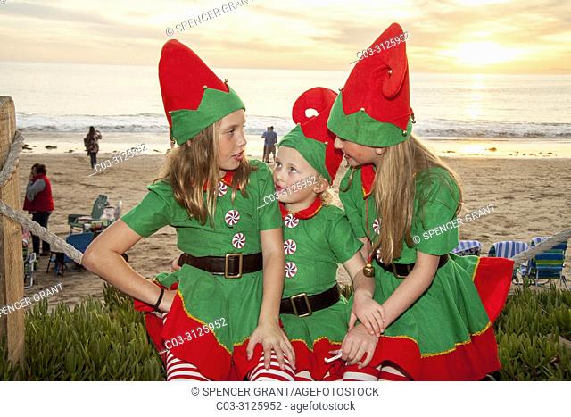 Three girls dressed as Christmas elves get into the holiday spirit at a seasonal celebration at sunset in Laguna Beach, CA