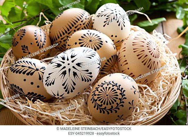 Easter eggs painted with wax in a basket, with birch branches in the background