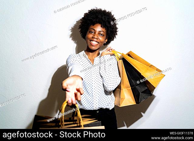 Woman stretching hand while carrying bags standing against white background