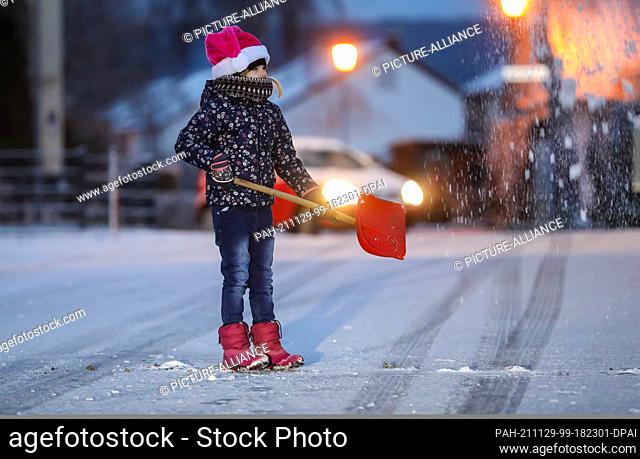 29 November 2021, Baden-Wuerttemberg, Riedlingen: Jule throws snow into the air with a snow shovel in the morning. Winter has arrived in Baden-Württemberg