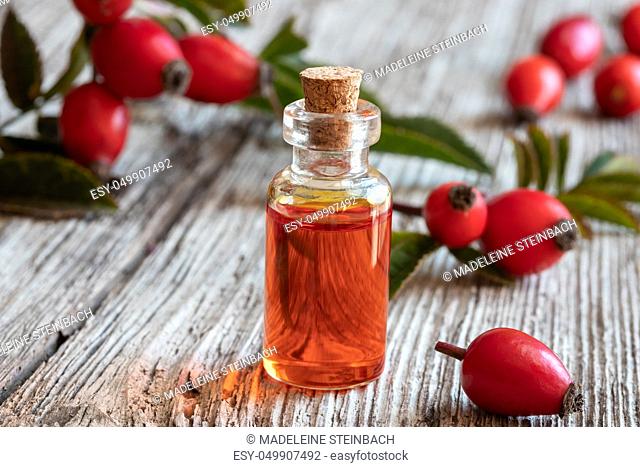 A bottle of rose hip seed oil with fresh berries and leaves