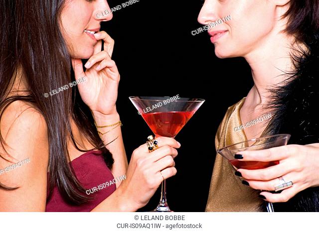 Two women holding cocktails, face to face, in nightclub