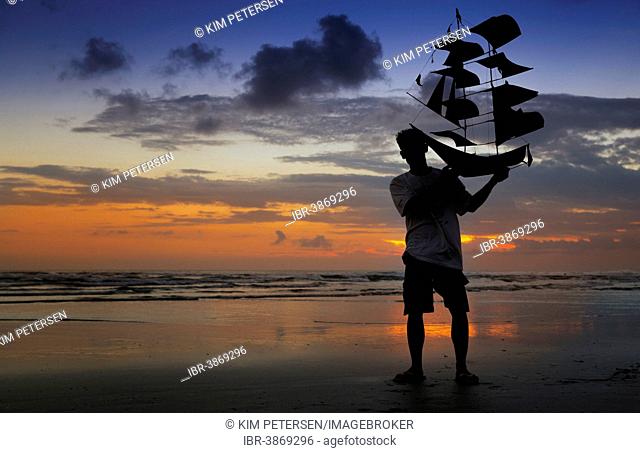 Silhouette of a man holding a kite shaped like a ship, Sanur Beach, Bali, Indonesia