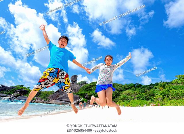 Father and daughter jumping with happy on beach near the sea under blue sky and cloud of summer at Koh Similan Island in Mu Ko Similan National Park