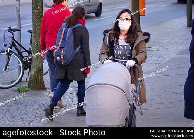26 March 2020, Berlin: A young woman with a stroller is wearing a protective mask and disposable gloves to protect against the novel corona virus