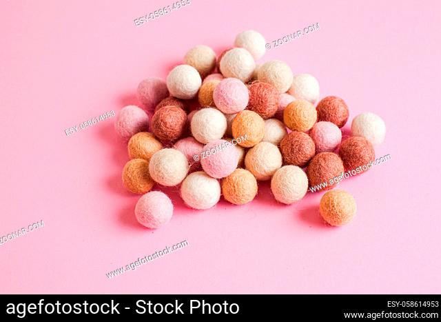 Large pale of small soft woolen balls on a pink background. Handmade felt balls of pastel colours