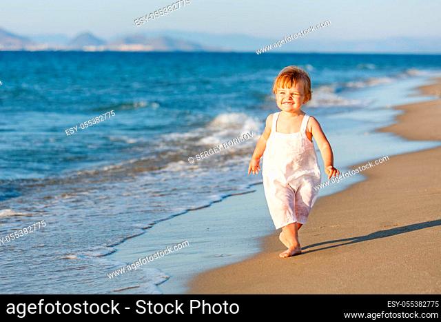 Little girl in white dress running on the beach