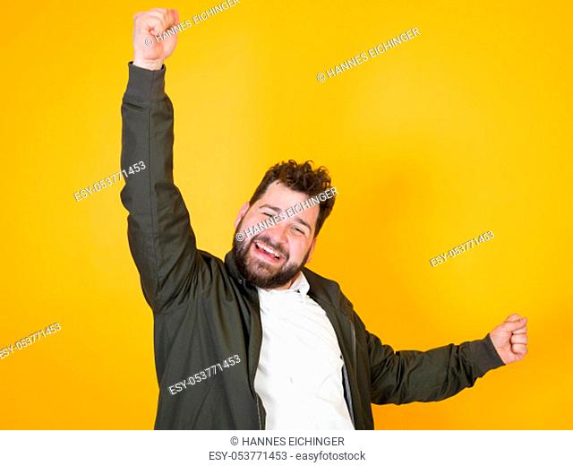 cool man with black beard and black hair is posing in front of orange background in the studio