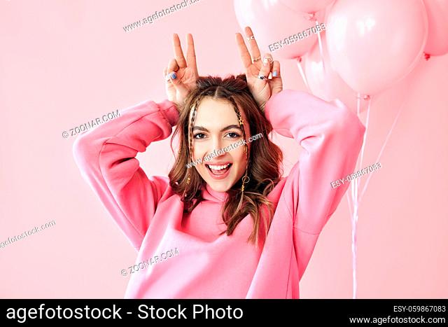 Young pretty woman have fun showing horns with fingers over head on pink background. Emotions concept