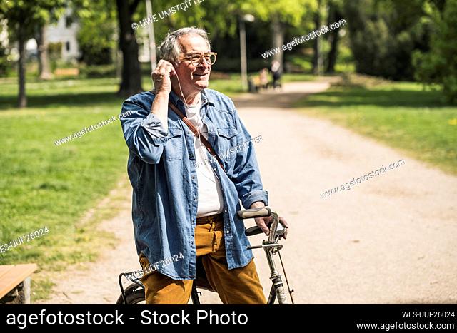 Smiling senior man wearing In-ear headphones with bicycle at park