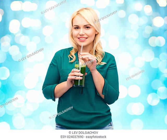 healthy eating, vegetarian food, diet, detox and people concept - smiling young woman drinking green vegetable juice or smoothie from glass over blue holidays...
