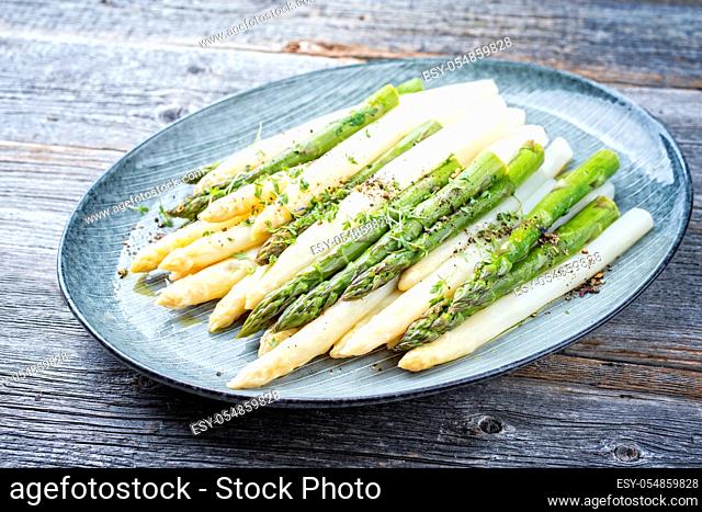 Traditional boiled white and green asparagus with butter sauce decorated with cress as closeup on a design plate on a wooden table