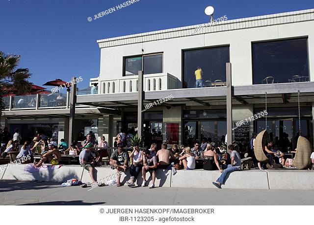 People sitting in and in front of a beach cafe in St. Kilda, a suburb of Melbourne, Victoria, Australia